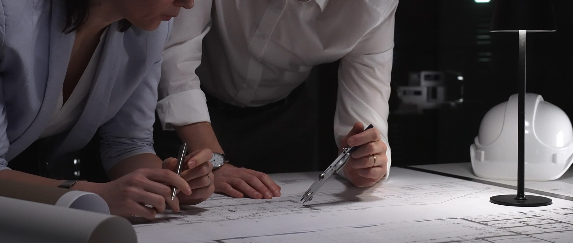 Two engineers leaning over technical drawings, reviewing plans together